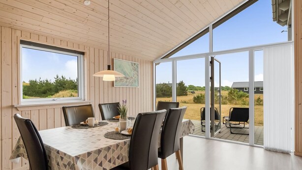 A dining area with a table set for four, surrounded by chairs, large windows, and a view of the outdoors. - "Clement" - 500m to the fjord by Interhome (Skjern)