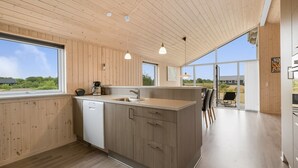 A modern kitchen with wooden paneling, a central island, and large windows offering a view of the outdoors. - "Clement" - 500m to the fjord by Interhome (Skjern)