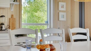 Una zona de comedor con una mesa blanca, dos sillas blancas, un plato, una copa, un croissant y una taza.