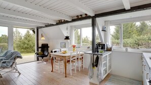 Una cocina moderna con armarios blancos, una zona de comedor con mesa y sillas de madera, y ventanas amplias que ofrecen vistas al exterior.