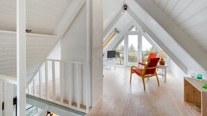 Una habitación amplia en el ático, con techos altos, ventanas grandes y suelo de madera.