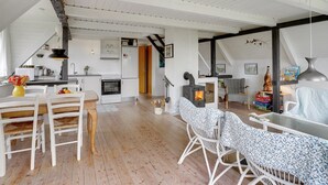 Un loft amplio con techo alto, vigas a la vista, una zona de cocina, una chimenea y un comedor con mobiliario de mimbre.