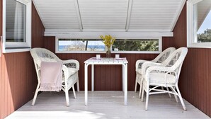 A covered outdoor seating area with wicker chairs and a table, wooden walls, and a view of the outdoors.