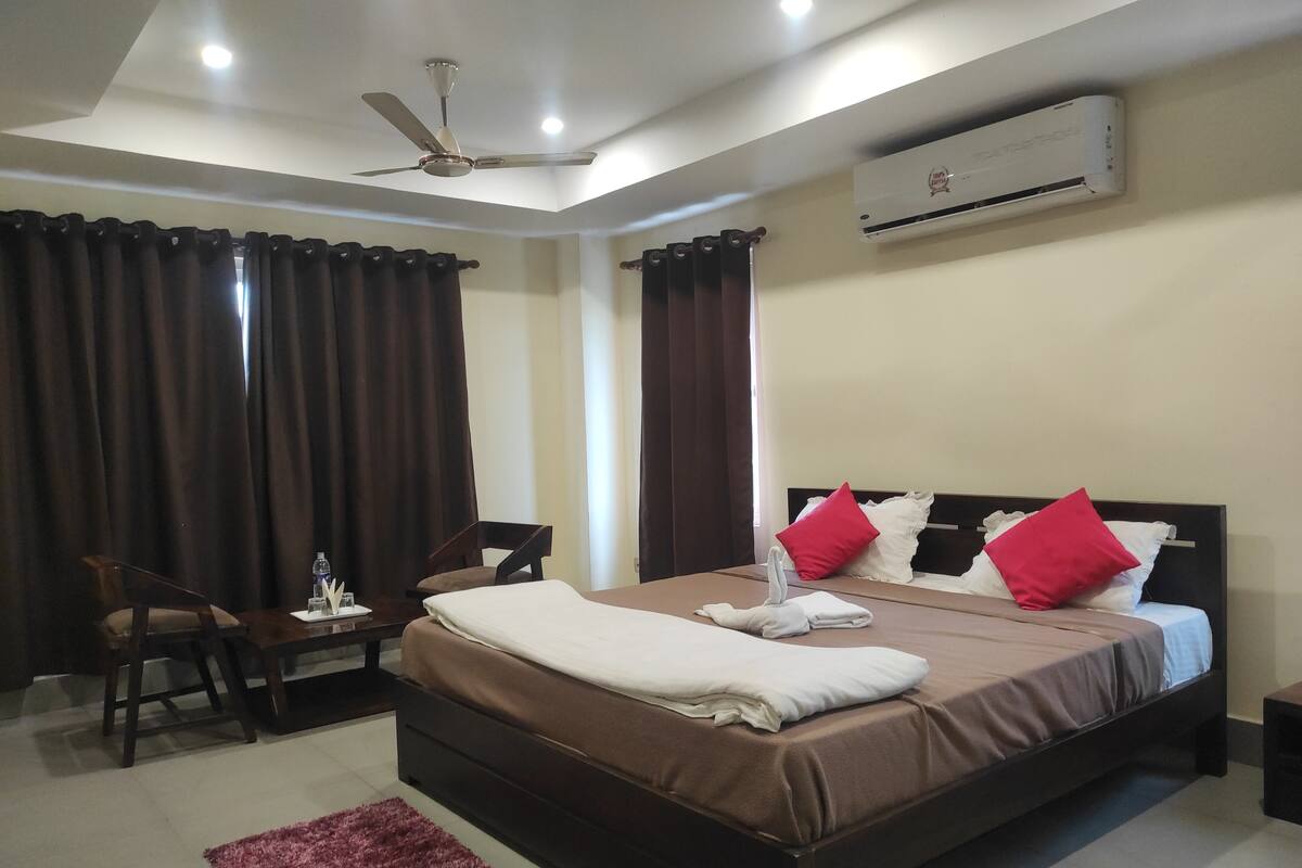 A hotel room with a bed, a desk, a chair, a ceiling fan, and an air conditioning unit.