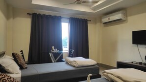 A hotel room with two beds, a desk, a TV, and an air conditioning unit. - Mayur Gardens (Sonapur)