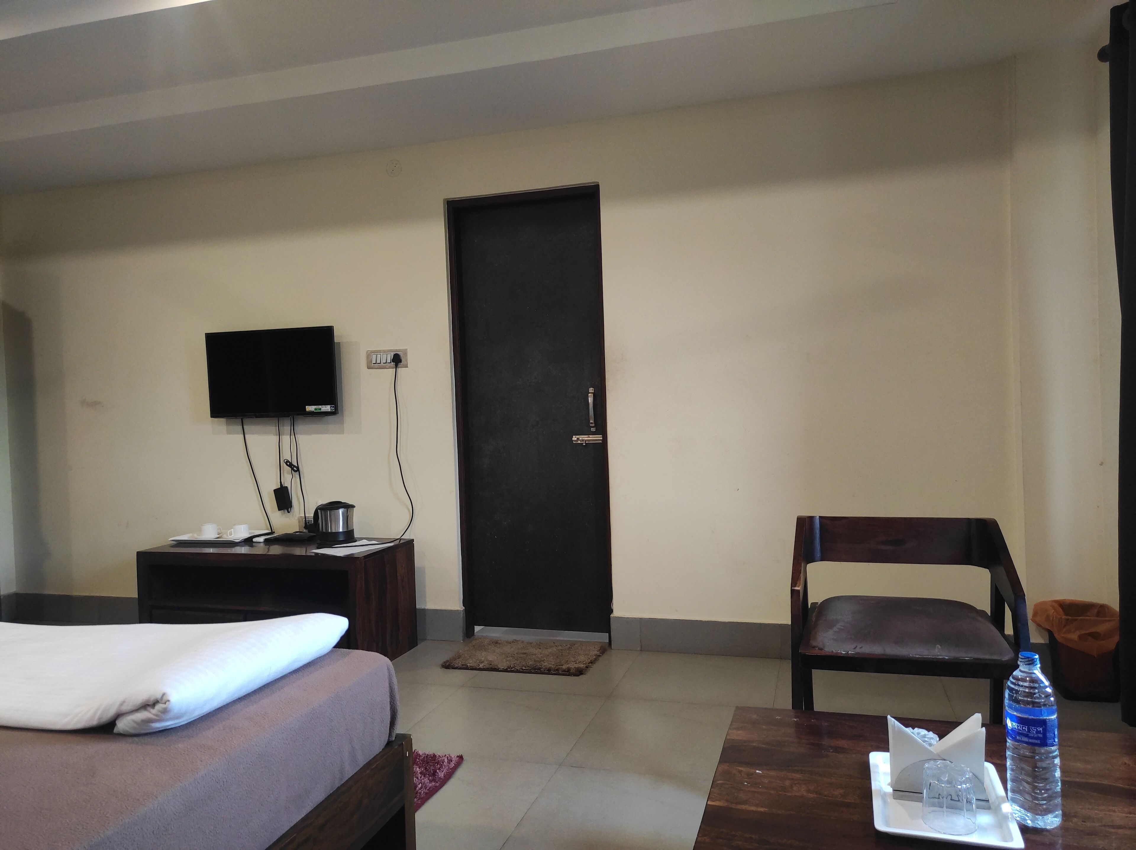 A hotel room with a bed, a desk, a chair, a television, and a water bottle.