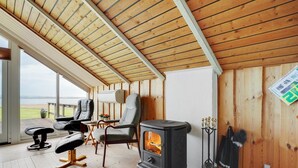 Une pièce chaleureuse avec un poêle à bois, des sièges confortables et une vue sur l’extérieur.