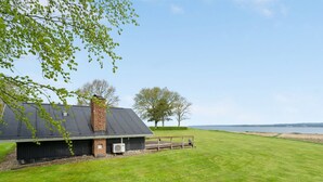 Un vaste champ herbeux et dégagé, avec un bâtiment doté d’une cheminée en briques et d’une zone abritée délimitée par une clôture en bois.