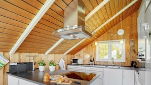Une cuisine moderne avec des poutres en bois, un îlot central, des armoires blanches et une fenêtre offrant une belle vue.