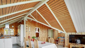 Un loft spacieux avec de hauts plafonds, des murs en bois, un coin repas avec une table et des chaises, une cuisine équipée d’appareils modernes et un téléviseur.