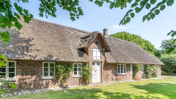 Een traditioneel bakstenen huis met rieten dak, een klein voortertje en een verzorgd gazon.