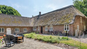 Een bakstenen gebouw met rieten dak, een patio met buitenmeubilair en fietsen die er staan.