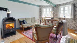 Een gezellige woonkamer met een open haard, een bank, stoelen, een tafel en behang met een patroon.