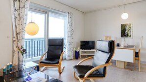 A modern living room with two leather chairs, a glass coffee table, a TV, and a balcony with curtains.