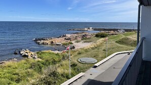 A coastal view with a rocky shoreline, a flag, and a paved walkway.