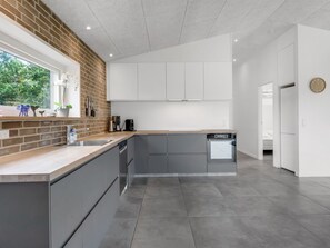 A modern kitchen with grey cabinets, a brick accent wall, and a window with decorative items. - "Asel" - 350m from the sea by Interhome (Grenaa)