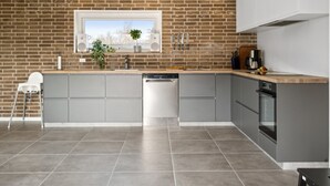 Une cuisine moderne avec des meubles gris, un mur en briques, une fenêtre offrant une belle vue et un lave-vaisselle.