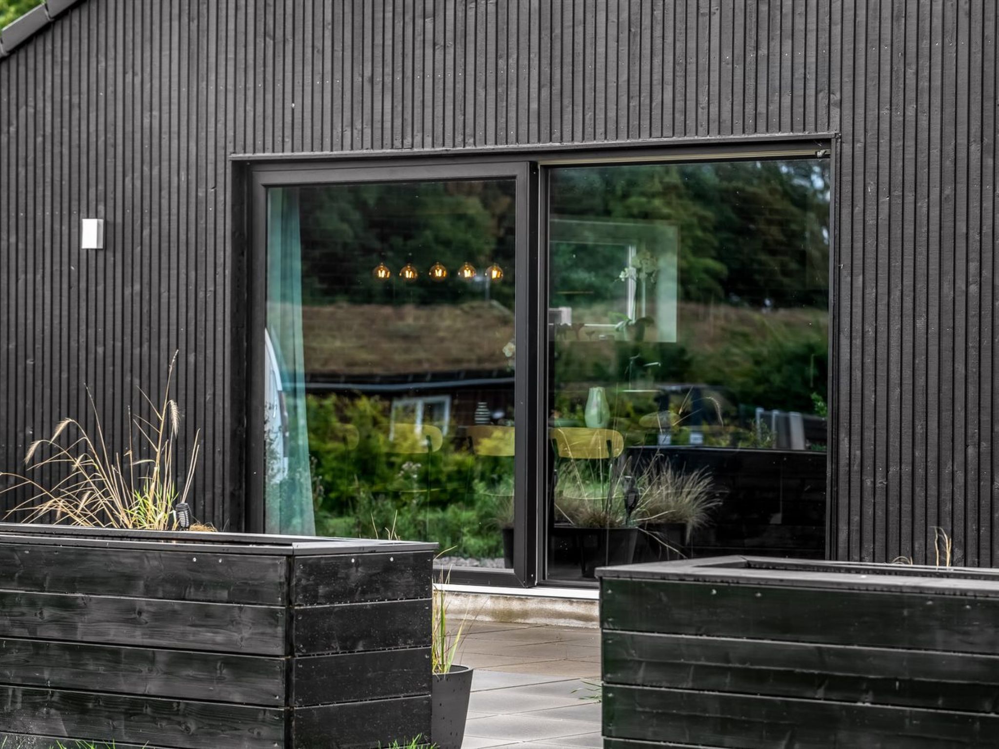 Un bâtiment moderne doté d’une grande porte et de grandes fenêtres en verre, entouré de verdure.