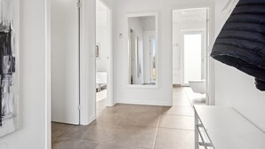 Un couloir aux murs blancs, doté d’un sol carrelé et d’une porte donnant sur une chambre à coucher.