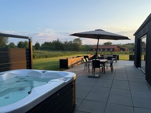 Un bain à remous, un espace salon extérieur et une vue sur une maison en arrière-plan.