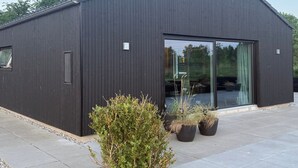 Un bâtiment moderne à l’extérieur sombre, doté de grandes portes vitrées et agrémenté de plantes en pot au premier plan.