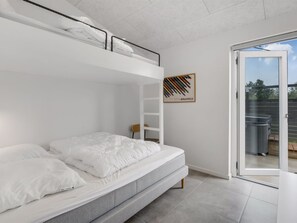 A modern bedroom with a bunk bed, a small chair, a framed picture on the wall, and a sliding glass door leading to an outdoor area.