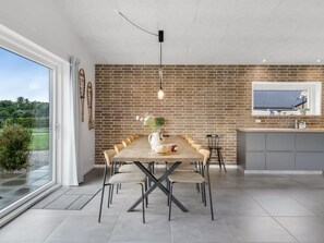 A modern kitchen with a brick wall, a dining table with chairs, a hanging light fixture, and a large window. - "Asel" - 350m from the sea by Interhome (Grenaa)