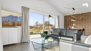 Un salon moderne avec une table basse en verre, un canapé noir et une grande fenêtre donnant sur l’extérieur.