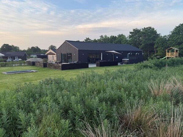 Une maison moderne dotée d’une grande terrasse, d’une piscine et d’une aire de jeux à l’arrière.