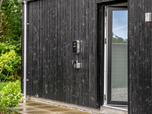 Un bâtiment moderne à l’extérieur noir, doté d’une porte coulissante en verre et d’un clavier de sécurité fixé au mur.