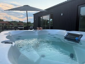 Ein Whirlpool mit Tisch und Stühlen, ein großer Sonnenschirm und ein modernes Gebäude mit großen Fenstern.