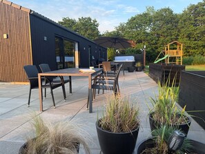 Une terrasse extérieure avec une table et des chaises, un barbecue et une aire de jeux pour enfants.