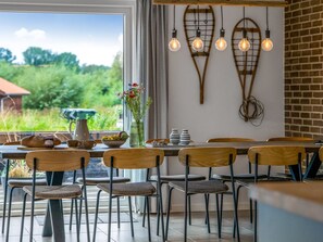 Un coin repas avec une table dressée pour quatre personnes, des chaises, un vase avec des fleurs et des luminaires suspendus.