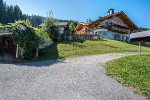 A rural house with a gravel driveway, wooden fences, and a hillside backdrop.
