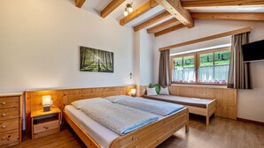 A wooden bed with a bench, a nightstand with a lamp, a painting of a forest, and a window with curtains. - Studio Apartment 'Urthalerhof Landhaus' with Mountain View, Shared Garden and Wi-Fi (Olang)
