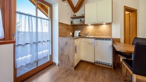 A compact kitchen with wooden cabinetry, a built-in dishwasher, and a dining area with a table and chairs. - Studio Apartment 'Urthalerhof Landhaus' with Mountain View, Shared Garden and Wi-Fi (Olang)