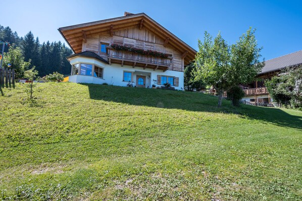 A two-story chalet with a wooden facade, a balcony with flowers, and a sloped roof.