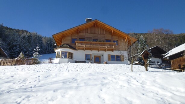 A wooden chalet with a balcony, surrounded by snow-covered ground and trees. - Studio Apartment 'Urthalerhof Landhaus' with Mountain View, Shared Garden and Wi-Fi (Olang)