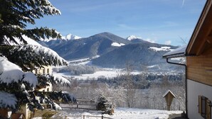 A snow-covered landscape with mountains in the background, a wooden building with a sloped roof, and a fenced yard. - Studio Apartment 'Urthalerhof Landhaus' with Mountain View, Shared Garden and Wi-Fi (Olang)