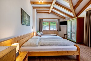 A bedroom with a wooden ceiling, a bed with white bedding, a bedside table with a lamp, a window with curtains, and a green cabinet.