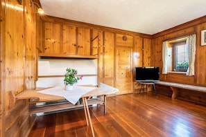 Een kamer met houten lambrisering, een houten bank, een tafel met een witte tafelkleed, een potplant en een televisie.