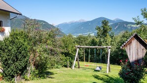 A house with a swing set in a garden, surrounded by mountains.