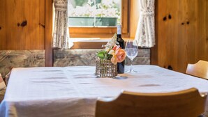 A wooden interior with a table set for two, featuring a bottle and a glass, and a window with curtains.