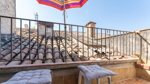 Una terraza en la azotea con suelo de baldosas, barandilla de metal y dos sillas de plástico blanco.
