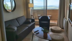 Una sala moderna con un sofá, una silla, una mesa con una planta y vistas al exterior a través de amplios ventanales.