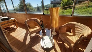 Una terraza de madera con sillas de mimbre, una mesa de vidrio y una planta en maceta.