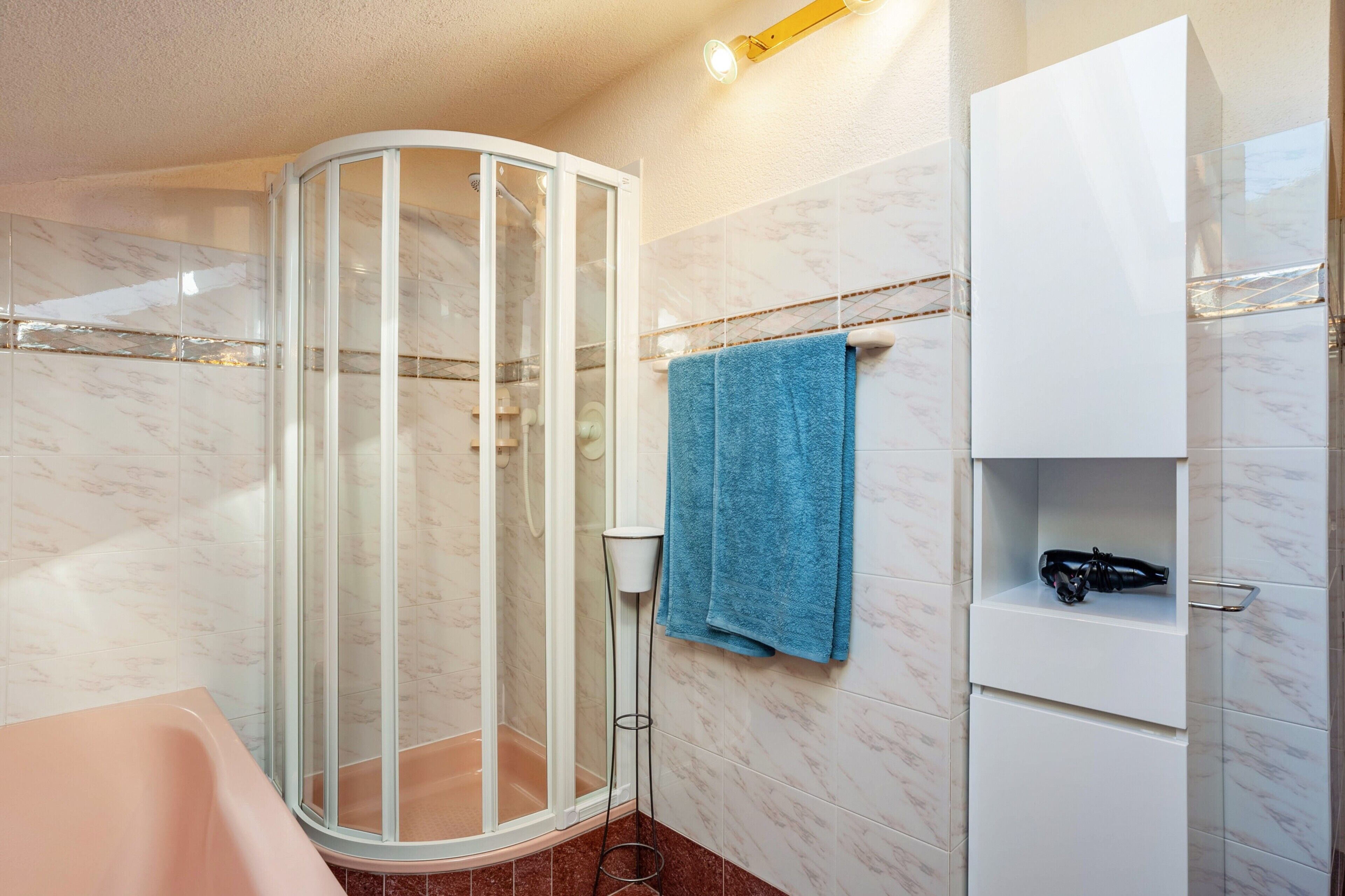 A bathroom with a glass shower enclosure, a white cabinet, and a blue towel.