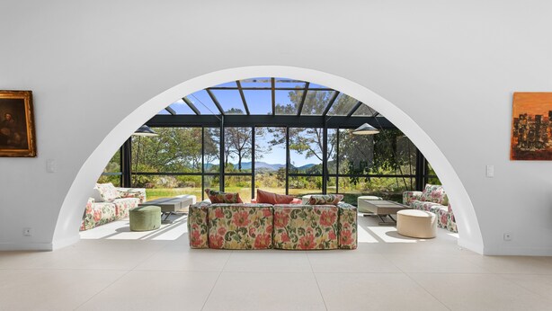 Ein geräumiges Zimmer mit einem großen Bogenfenster, einer floralen Sofagarnitur und Blick auf einen Garten.