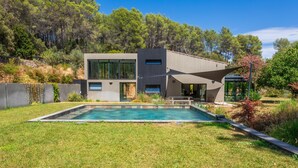 Ein modernes Haus mit Schwimmbad, umgeben von einem gepflegten Rasen und Bäumen.
