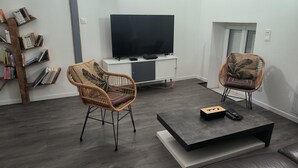 Un saló modern amb dues cadires de vimet, un televisor de pantalla plana, una taula de centre i una estanteria.